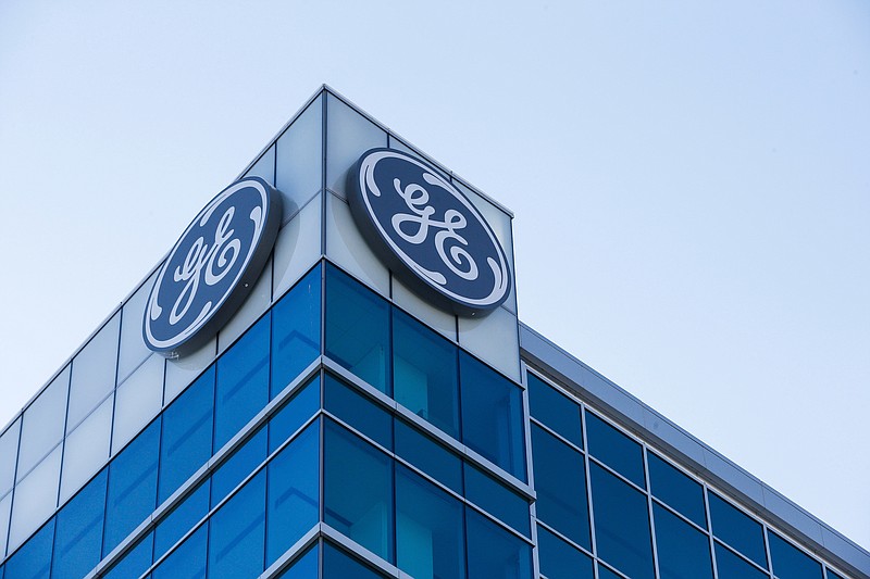 FILE- In this Jan. 16, 2018, file photo, the General Electric logo is displayed at the top of their Global Operations Center in the Banks development of downtown Cincinnati. A year after taking over an ailing American conglomerate, CEO John Flannery is calving off larger chunks of General Electric, spinning off its health care business and selling its stake in the oil services company, Baker Hughes. (AP Photo/John Minchillo, File)