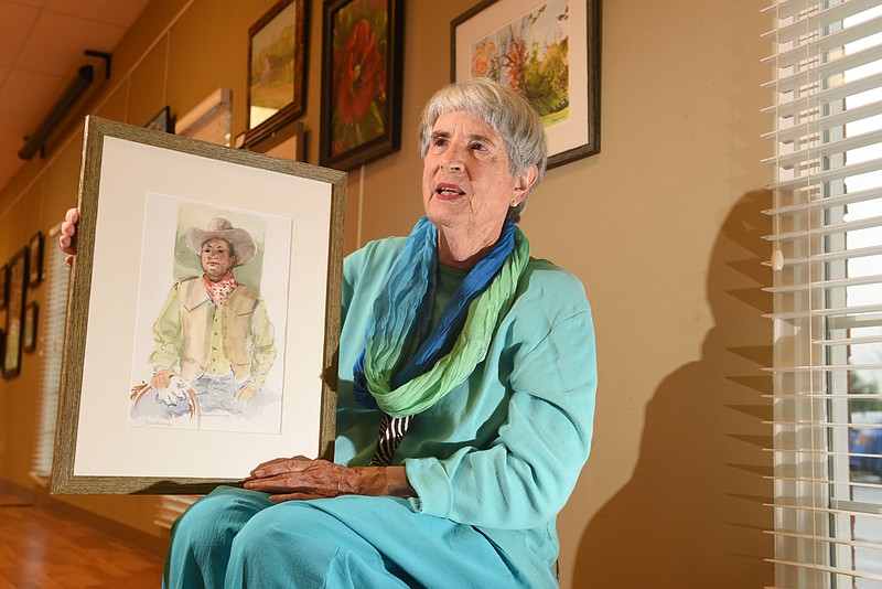 Artist Gerri Bauhaus Williams is seen with two of her works inside the North River Civic Center, where she teaches. Her works include "Tennessee Cowhand," which she's holding, and "Valleybrook Golf Course Pond," hanging top right. Both works are traditional watercolor.