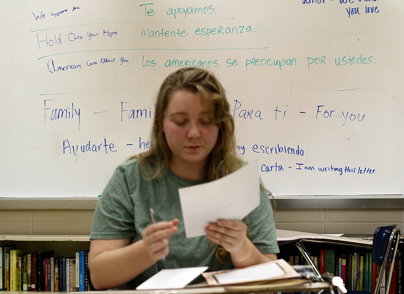 Phrases of inspiration and their Spanish translation are seen on the board behind former student Hannah Stone as she writes a letter of hope to be delivered to immigrants at the boarder in Sally White's classroom at Chattanooga Central High School on Wednesday, June 27, 2018 in Harrison, Tenn. White, a teacher at Central, helped organize the event for current and former students to write letters of support to immigrants. White will be delivering the letters along with donations and funds.