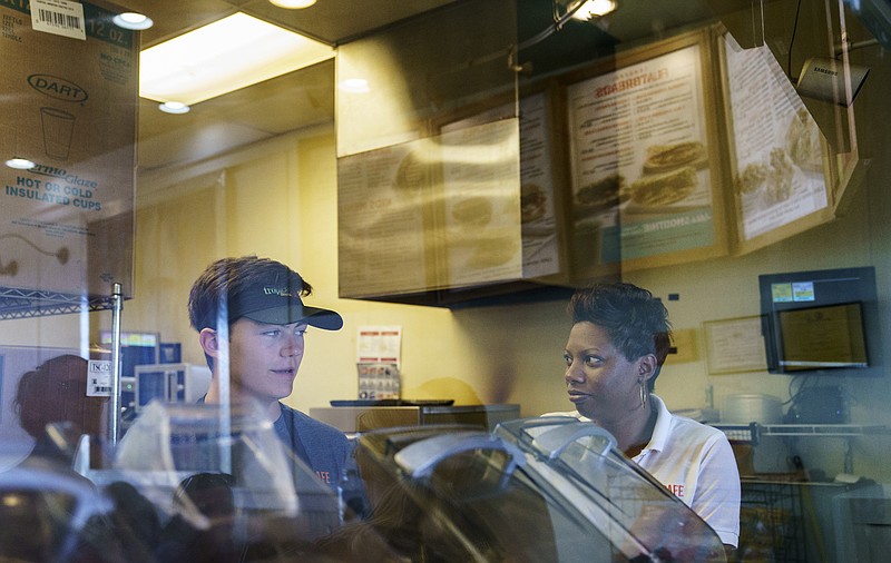 In this Friday, June 29, 2018, photo Nicole Drake, co-owner of Tropical Smoothie Cafe franchises in Gainesville and Ashburn, Va. with her husband Dennis Drake, talks with employee Matthew Dumm, left, in the Ashburn, Va., store. (AP Photo/Carolyn Kaster)
