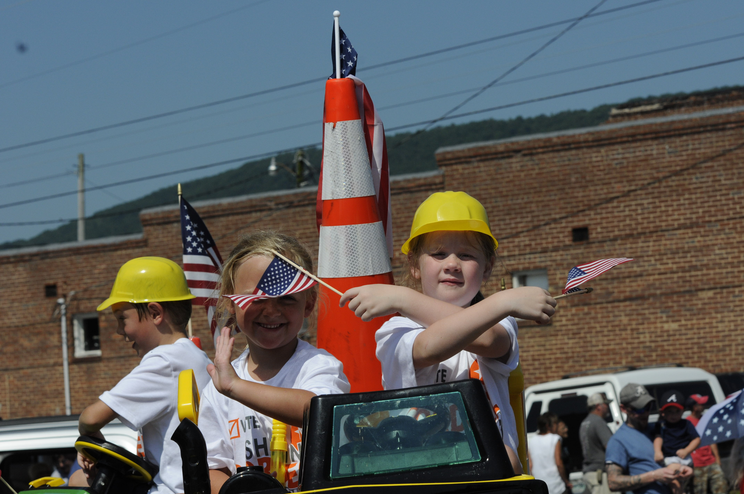 Zoe Rigsby, right, waves two American flags alongside her friend Halley Summers Wednesday atop a Shawn Cordell for Road Supervisor float during the annual Fourth of July parade in Dunlap.