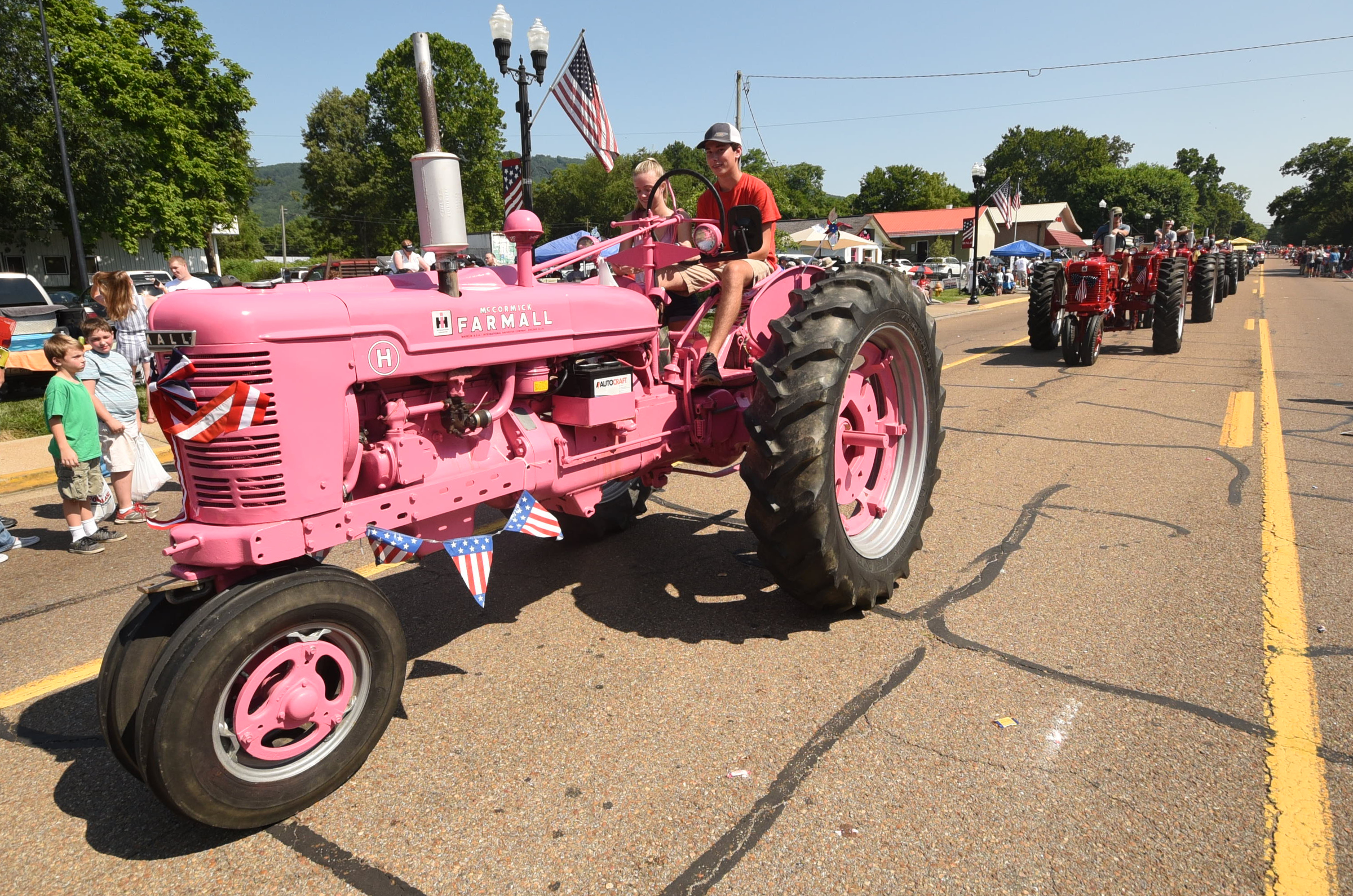 Eli Wash drives a pink Farmall tractor down Rankin Avenue Wednesday during the annual Fourth of July parade. Taylor Stepanske rides with him as nearly a dozen tractors fall in behind.