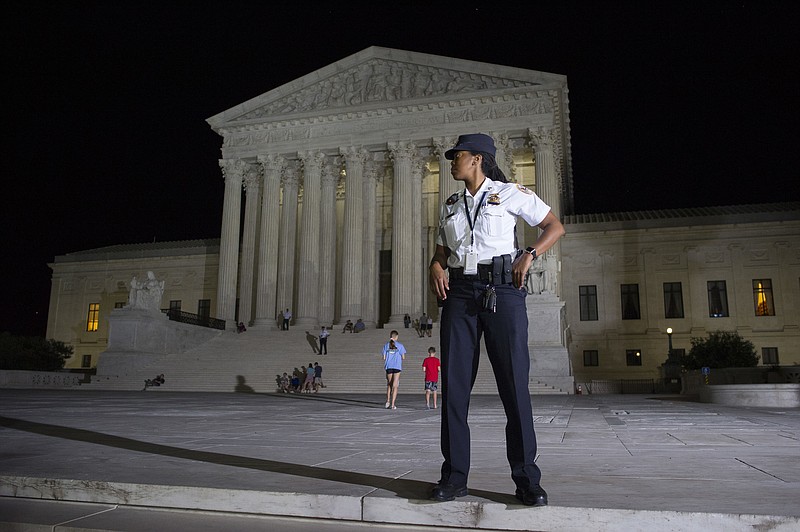 A Supreme Court Police officer stands watch as a protesters demonstrate in front of the Supreme Court in Washington, Monday, July 9, 2018, after President Donald Trump announced Judge Brett Kavanaugh as his Supreme Court nominee.. (AP Photo/Cliff Owen)

