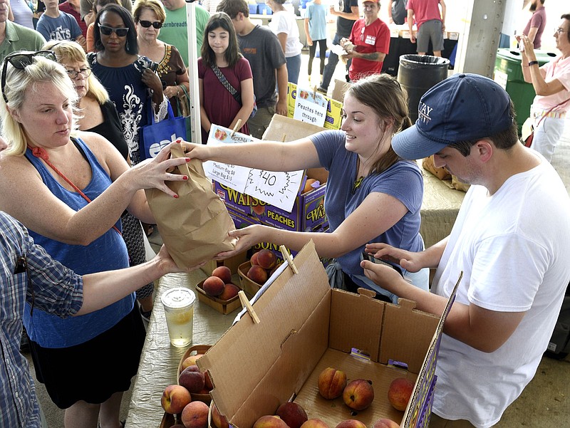 From right, Ben Lee totals a sale while Kathleen Sharpe serves a customer as the duo from Watsonia Farms of Monetta, South Carolina strive to keep up with demand at last year's Peach Festival at Chattanooga Market.