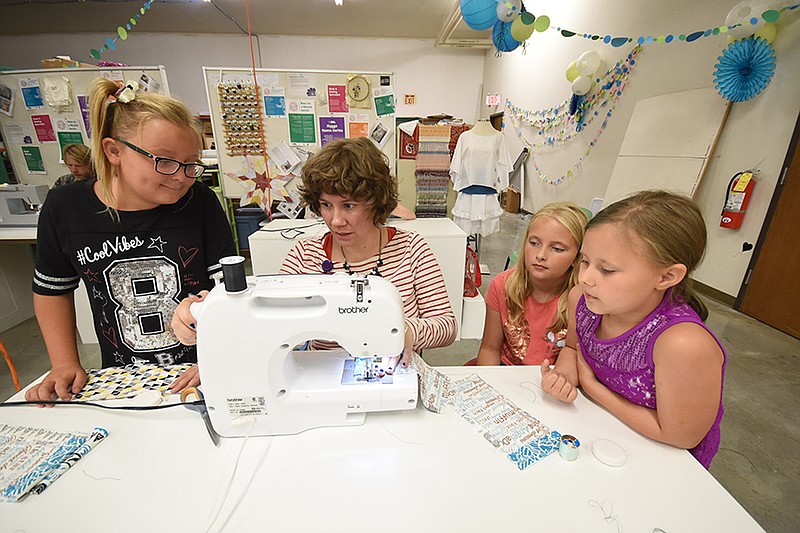 Staff photo by Tim Barber / All the girls listen to Sew What instructor Megan Emery, second from left, as she reaches to adjust a machine during class Thursday evening at The Public LIbrary. From left are, Arissa Kenner, Emery, Emmalee Dittmar and Lailah Lockwood.