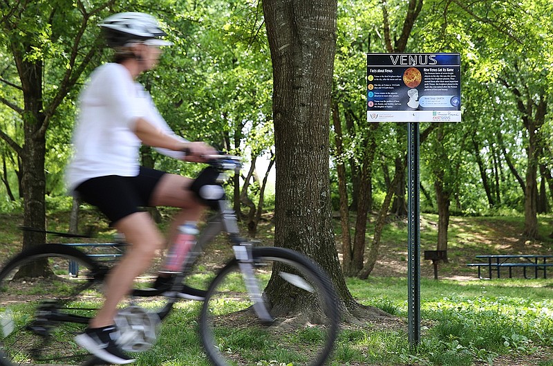 A biker rides by a sign about the planet Venus on the Chattanooga Girls Leadership Academy's Solar System Walking trail along the Tennessee Riverwalk.