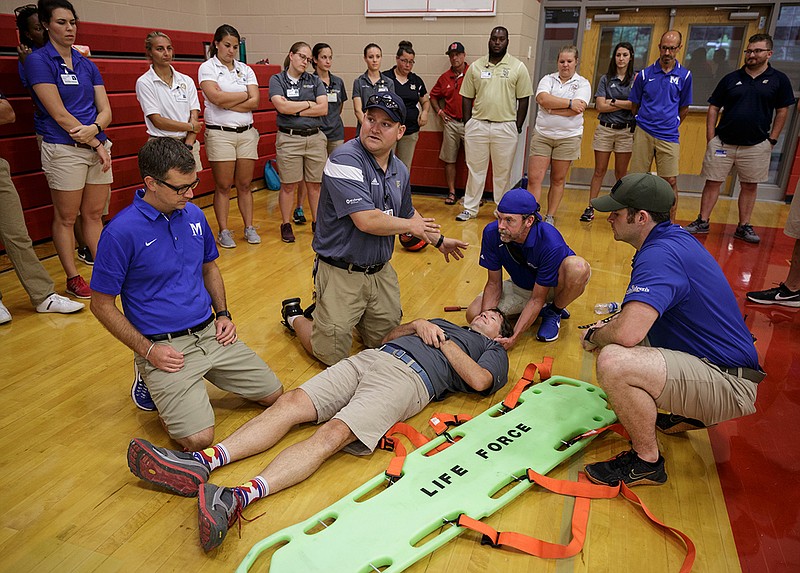 Paramedic Kevin Gebicke with Erlanger Lifeforce's Event Medicine crew, center, explains how to move a patient onto a backboard during a backboard-immobilization workshop hosted by Erlanger Hospital at Signal Mountain Middle High School on Friday, July 27, 2018, in Signal Mountain, Tenn. Athletic trainers with area high schools got hands-on training on how to properly move an injured athlete onto a backboard for transport.