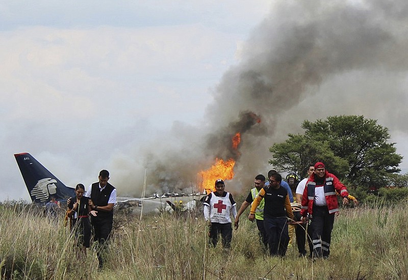 In this photo released by Red Cross Durango communications office, Red Cross workers and rescue workers carry an injured person on a stretcher, right, as airline workers, left, walk away from the site where an Aeromexico airliner crashed in a field near the airport in Durango, Mexico, Tuesday, July 31, 2018.