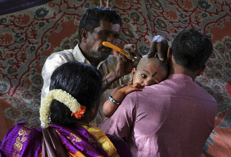 FILE- In this Aug. 8, 2015 file photo, devotees of Hindu god Muruga get the head of their child shaved as part of rituals at a temple in Bangalore, India. Indian police say three men posing as customers robbed a small New Delhi workshop and fled with a valuable commodity: Hair. Lots of hair. Hair is big business in India, estimated to bring in more than $300 million a year, with wigs and hair extensions exported around the world. Much of the hair is collected at Hindu temples in South India where devotees have their heads shaved as a form of religious sacrifice. (AP Photo/Aijaz Rahi, File)