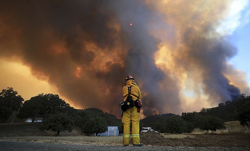 A tower of smoke pours from Cow Mountain as Burney, California firefighter Bob May keeps a watch on surrounding vegetation for spot fires during a wildfire off Scotts Valley Road, Thursday, Aug. 2, 2018, near Lakeport, Calif. (Kent Porter /The Press Democrat via AP)