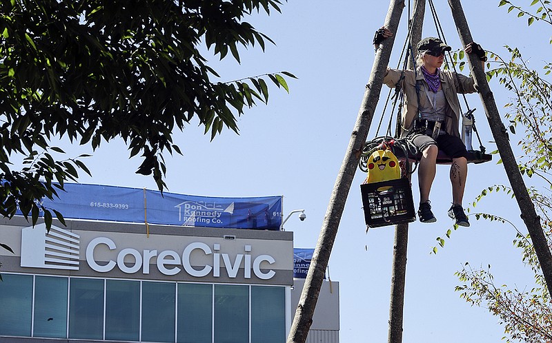 Julie Henry sits on a suspended platform as she protests outside the headquarters of CoreCivic Monday, Aug. 6, 2018, in Nashville, Tenn. 