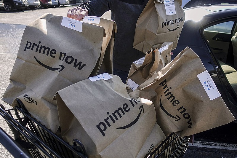 FILE- In this Feb. 8, 2018, file photo, Amazon Prime Now bags full of groceries are loaded for delivery by a part-time worker outside a Whole Foods store in Cincinnati. Amazon, known for bringing items to shoppers' homes, is adding a curbside pickup option at Whole Foods for Prime members. The Whole Foods move announced Wednesday, Aug. 8, 2018, is the latest by Seattle-based Amazon.com Inc. since it took control of the grocery chain a year ago. (AP Photo/John Minchillo)