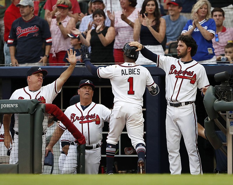 The Atlanta Braves' Ozzie Albies is greeted at the dugout entrance by, from left, hitting coach Kevin Seitzer, manager Brian Snitker and teammate Dansby Swanson after scoring on a Nick Markakis double in the first inning of Friday night's 10-1 win against the Milwaukee Brewers.