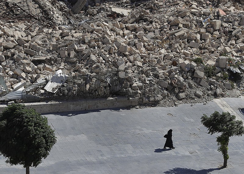 In this photo taken on Thursday, Aug. 16, 2018, a woman walks past the remnants of destroyed buildings in the city of Aleppo, Syria. Russian air defense assets in Syria claim to have downed 45 drones targeting their main base in the country, its military said Thursday, after an attack by the Islamic State group on a Syrian army base a day earlier killed seven troops. (AP Photo/Sergei Grits)