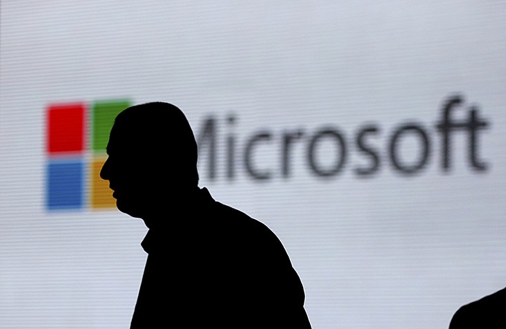 FILE - In this Nov. 7, 2017, file photo, a man is silhouetted as he walks in front of Microsoft logo at an event in New Delhi, India.