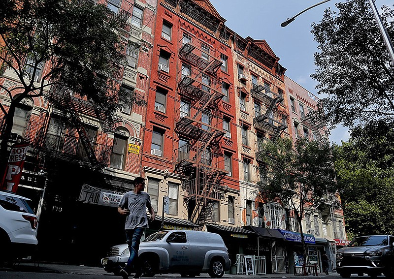 A pedestrian crosses in front of an apartment building at 172 Rivington Street, second from left, Monday, Aug. 27, 2018, in New York. The building is one of three in New York City once owned by former Donald Trump lawyer Michael Cohen and business partners in which they filed false documents to the city claiming they were empty. A tenants watchdog group says the false filings helped Cohen avoid strict oversight of construction work and allowed him to chase tenants out. (AP Photo/Julie Jacobson)