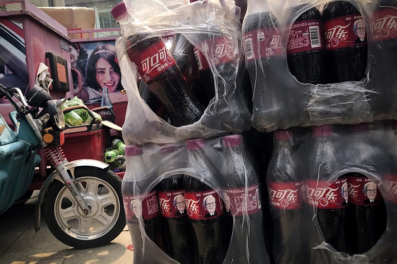 Bottles of Cherry Coca-Cola with portraits of Berkshire Hathaway Chairman and CEO Warren Buffett are stacked near a dispatch rider's bike in Beijing, Tuesday, Sept. 11, 2018. China on Monday promised retaliation if U.S. President Donald Trump escalates their tariff battle, raising the risk Beijing might target operations of American companies as it runs out of imports for penalties. (AP Photo/Andy Wong)