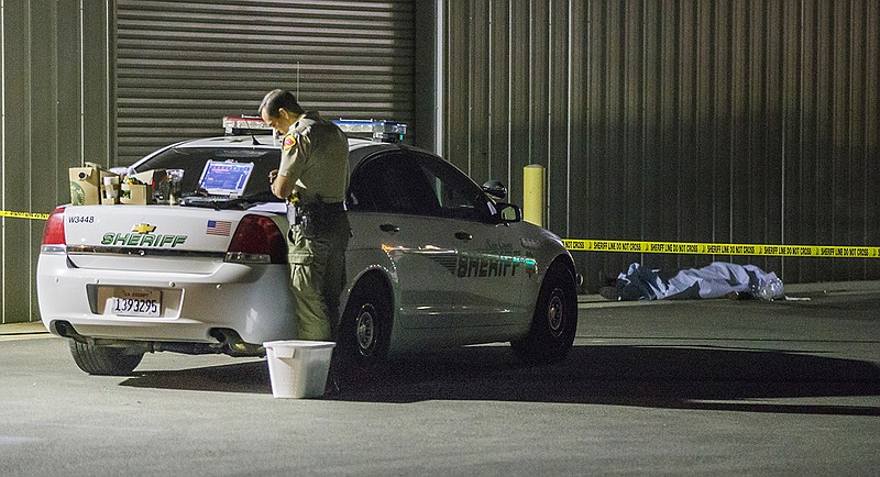 A Kern County sheriff's deputy stands near an area where a shooting victim lies, Wednesday, Sept. 12, 2018, in Bakersfield, Calif. A gunman killed five people, including his wife, before turning the gun on himself, authorities said. (Felix Adamo/The Bakersfield Californian via AP)