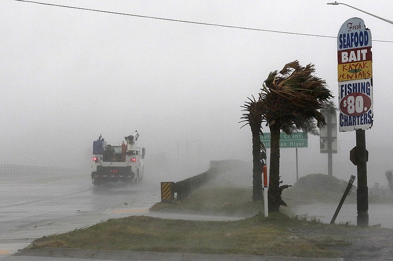 A work truck drives on Highway 24 as the wind from Hurricane Florence blows palm trees in Swansboro, N.C., on Thursday, Sept. 13, 2018. (AP Photo/Tom Copeland)