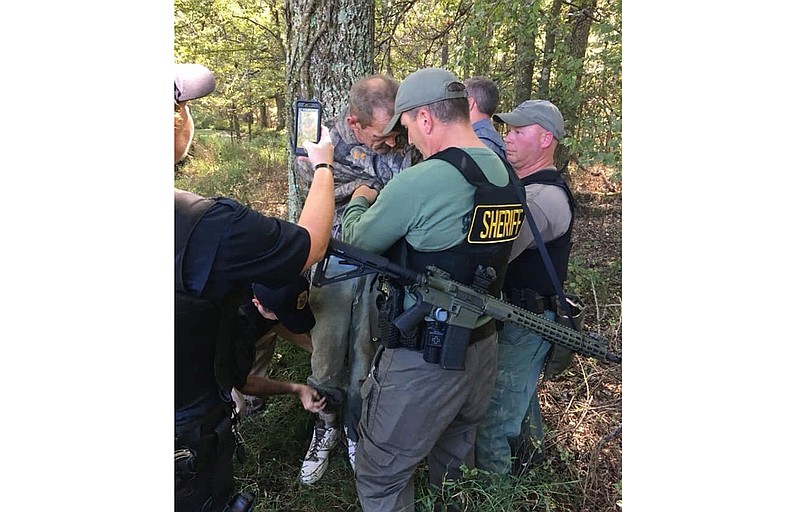 This photo provided by The Tennessee Bureau of Investigation shows law enforcement agents holding Kirby Wallace in custody on Friday, Oct. 5, 2018 in Tennessee. Wallace is wanted on multiple charges after being accused of attacking a couple and setting their house on fire, killing the wife and seriously injuring the husband. He's also accused of fatally shooting a man Monday and stealing his truck. (The Tennessee Bureau of Investigation via AP)