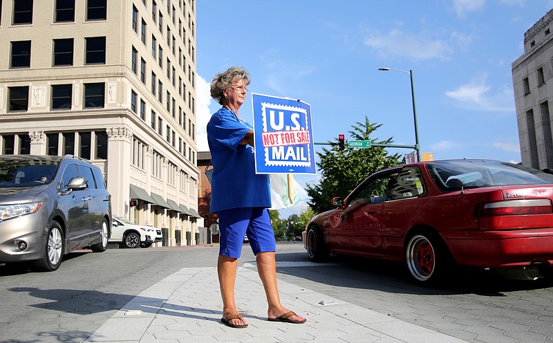 Cathie Cox holds up a sign reading "U.S. Mail Not For Sale" and hands out fliers to passersby Monday, October 8, 2018 along M.L. King Boulevard in Chattanooga, Tennessee. The rally was held in opposition to President Donald Trump's plan to privatize the post office.