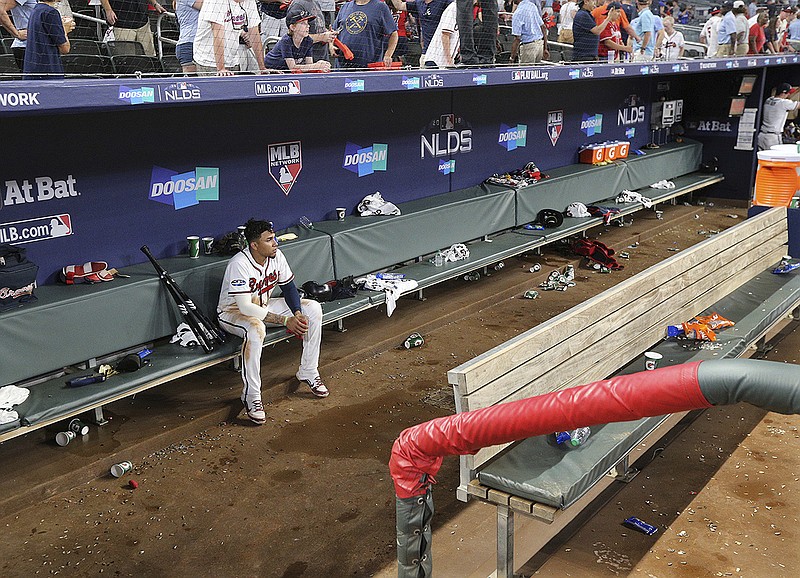 Atlanta Braves' Johan Camargo sits in the dugout alone, the last to leave, while watching the Los Angeles Dodgers celebrate a victory in Game 4 of baseball's National League Division Series, Monday, Oct. 8, 2018, in Atlanta. (Curtis Compton/Atlanta Journal-Constitution via AP)