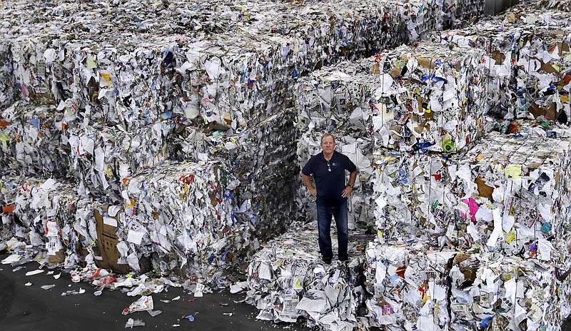 In this Thursday, Sept. 6, 2018, photo, Ben Harvey, an owner at EL Harvey & Sons, a waste and recycling company, poses on bundles of residential mixed fiber, comprised of a variety of paper and cardboard, in Westborough, Mass. The company is currently stacking and holding onto about 2,500 tons of the material, which is awaiting a destination where a recycler will process the bundles. Recycling programs across the United States are shutting down or scaling back because of a global market crisis blamed on contamination at the curbside bin. (AP Photo/Charles Krupa)