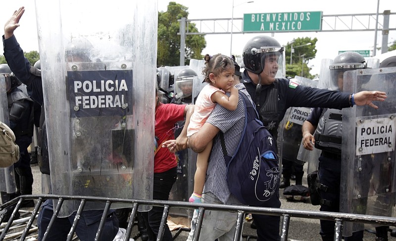 A Honduran migrant family is allowed to pass through to safety by Mexican Federal Police in riot gear, at the border crossing in Ciudad Hidalgo, Mexico, Friday, Oct. 19, 2018. Central Americans traveling in a mass caravan broke through a Guatemalan border fence and streamed by the thousands toward Mexican territory, defying Mexican authorities' entreaties for an orderly migration and U.S. President Donald Trump's threats of retaliation. (AP Photo/Moises Castillo)