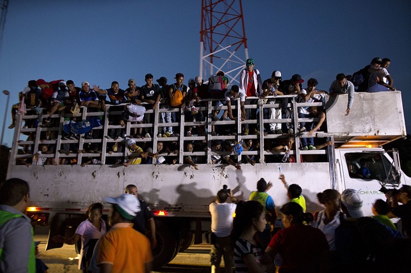 Men pass up water to Central Americans riding on the back of a truck while other migrants wait for rides, as a thousands-strong caravan of Central American makes its way toward the U.S. border, north of Pijijiapan, Mexico, at dawn on Friday, Oct. 26, 2018. Many migrants said they felt safer traveling and sleeping with several thousand strangers in unknown towns than hiring a smuggler or trying to make the trip alone.(AP Photo/Rebecca Blackwell)

