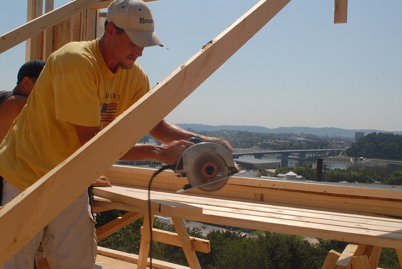 A construction worker saws wood for a home on a steep slope overlooking the Tennessee River.

