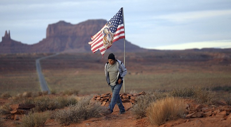 In this Thursday, Oct. 25, 2018, photo, Brandon Nez displays his flag at near his jewelry stand in Monument Valley, Utah, where tourists stand the highway to recreate a famous running scene from the movie "Forest Gump.". As Native American tribes around the country fight for increased access to the ballot box, Navajo voters in one Utah county could tip the balance of power in the first general election since a federal judge ordered overturned their voting districts as illegally drawn to minimize native voices. (AP Photo/Rick Bowmer)

