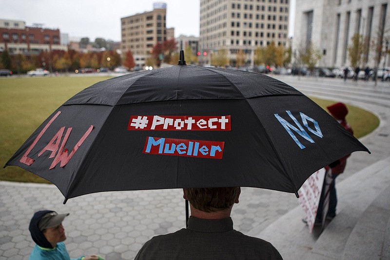Staff photo by C.B. Schmelter / Frank Gibson stands under an umbrella in Chattanooga's Miller Park with slogans of support for special counsel Robert Mueller while waiting for a MoveOn "No One is Above the Law" protest to start last week.