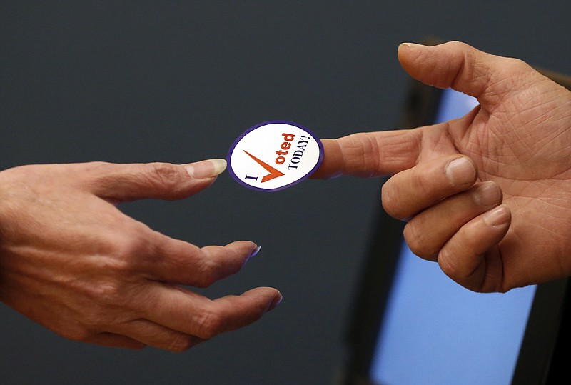 An election official hands an "I voted today" sticker to a woman after she cast her ballot in the mid-term election. (AP Photo/Robert F. Bukaty)