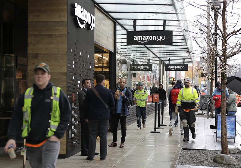 In this Nov. 9, 2018 photo, construction workers mix with the noon lunch-hour crowd outside an Amazon Go store in downtown Seattle.  As Amazon turns its attention to setting up new homes in Long Island City in New York  and Arlington, Va., experts and historians in Seattle say both places can expect a delicate relationship with the world’s hottest online retailer.  (AP Photo/Ted S. Warren)