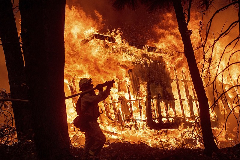 In this Nov. 9, 2018 file photo, firefighter Jose Corona sprays water as flames from the Camp Fire consume a home in Magalia, Calif. A massive new federal report warns that extreme weather disasters, like California's wildfires and 2018's hurricanes, are worsening in the United States. The White House report quietly issued Friday, Nov. 23 also frequently contradicts President Donald Trump. (AP Photo/Noah Berger, File)