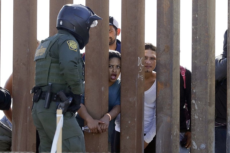Migrants from Central America yell through a border wall at a U.S. Border Patrol agent after he pulled down a banner Sunday, Nov. 25, 2018, in San Diego. Migrants approaching the U.S. border from Mexico were enveloped with tear gas Sunday after a few tried to breach the fence separating the two countries. (AP Photo/Gregory Bull)

