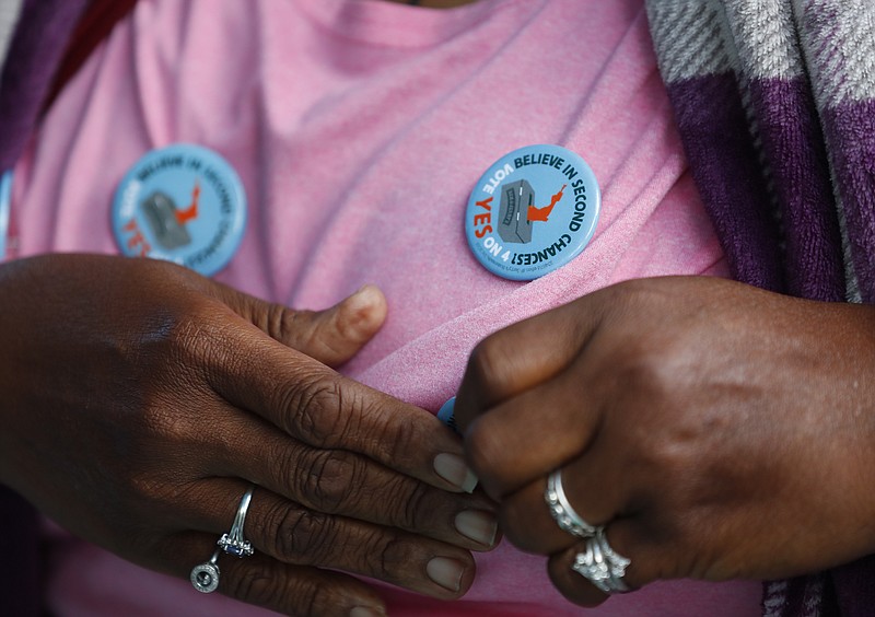 In this Oct. 22, 2018 photo, Yvette Demerit puts on Amendment 4 button at the Ben & Jerry's "Yes on 4" Truck where people learned about the amendment and ate free ice cream at Charles Hadley Park in Miami. Amendment 4 asks voters to restore the voting rights of people with past felony convictions. (AP Photo/Wilfredo Lee)