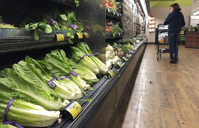 In this Nov. 20, 2018, file photo, romaine lettuce sits on the shelves as a shopper walks through the produce area of an Albertsons market in Simi Valley, Calif. After repeated food poisoning outbreaks linked to romaine lettuce, the produce industry is confronting the failure of its own safety measures in preventing contaminations. The latest outbreak underscores the challenge of eliminating risk for vegetables grown in open fields and eaten raw. It also highlights the role of nearby cattle operations and the delay of stricter federal food safety regulations. (AP Photo/Mark J. Terrill, File)