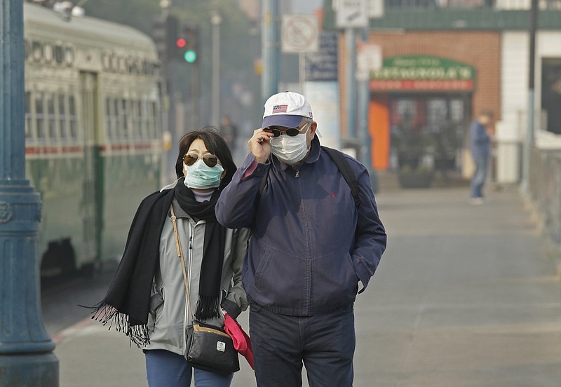 In this Nov. 16, 2018, file photo, a couple wears masks while walking at Fisherman's Wharf through smoke and haze from wildfires in San Francisco. From air pollution triggered by wildfires that caused people in Northern California to don breathing masks to increased asthma attacks that send children to the hospital, medical experts said climate change is hurting people's bodies. (AP Photo/Eric Risberg, File)