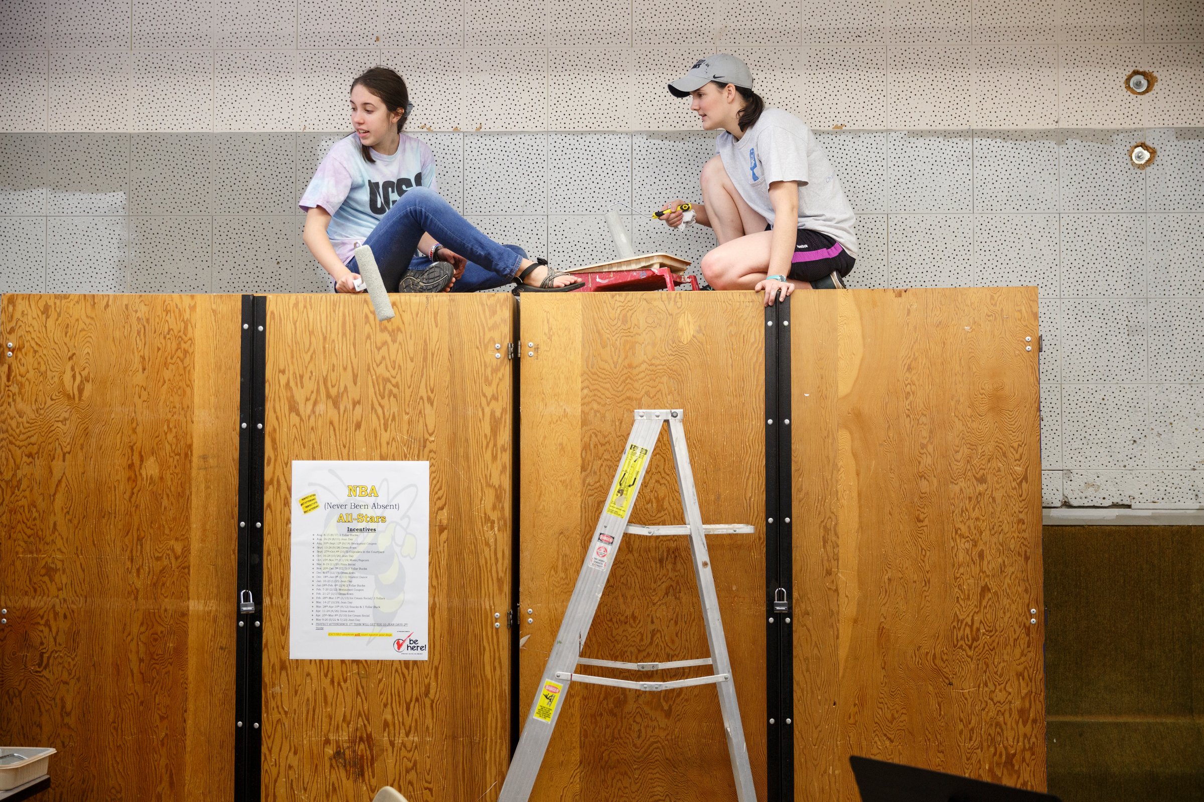 Jenny Etheridge, left, and Charity Cooke sit atop cabinets to paint the band room walls.