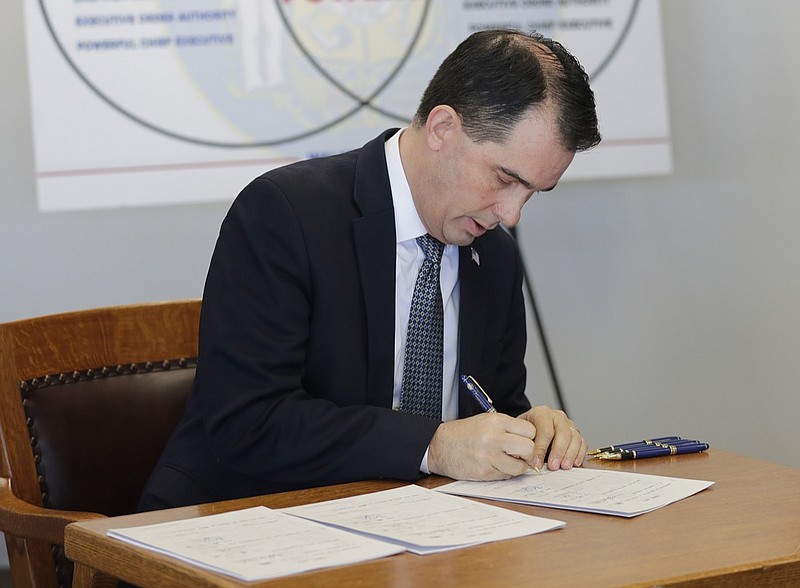 Gov. Scott Walker signs three pieces of legislation during a news conference Friday, Dec. 14, 2018 in Green Bay, Wis. Walker signed a sweeping package of Republican-written legislation Friday that restricts early voting and weakens the incoming Democratic governor and attorney general, brushing aside complaints that he is enabling a brazen power grab and ignoring the will of voters. (Jim Matthews/The Green Bay Press-Gazette via AP)