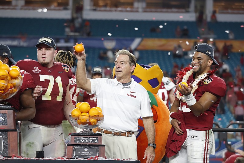 Alabama football coach Nick Saban tosses an orange early Sunday morning after the Crimson Tide's 45-34 victory over Oklahoma in the Orange Bowl on Saturday night in Miami Gardens, Fla. Alabama center Ross Pierschbacher (71) and quarterback Tua Tagovailoa (13) look on.
