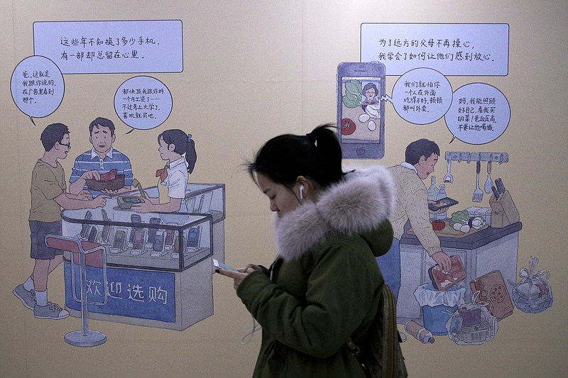 A woman browses her iPhone as she walks by a mural depicting an iPhone and Chinese people buy smartphone to communicate with family members, at a subway station in Beijing, Thursday, Jan. 3, 2019. Apple Inc.’s $1,000 iPhone is a tough sell to Chinese consumers who are jittery over an economic slump and a trade war with Washington. The tech giant became the latest global company to collide with Chinese consumer anxiety when CEO Tim Cook said iPhone demand is waning, due mostly to China. Weak consumer demand in the world’s second-largest economy is a blow to industries from autos to designer clothing that are counting on China to drive revenue growth. (AP Photo/Andy Wong)