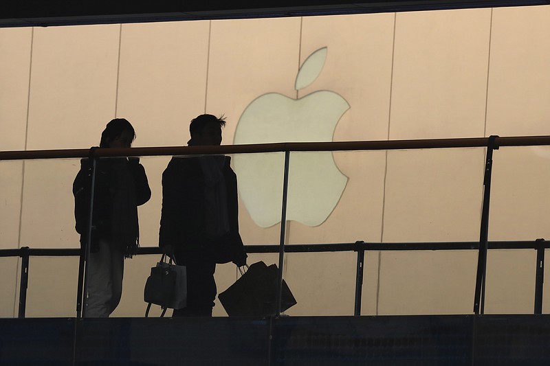 In this Thursday, Jan. 3, 2019, photo, shoppers pass by the Apple store logo at a shopping mall in Beijing. A U.S. delegation led by deputy U.S. trade representative, Jeffrey D. Gerrish arrived in the Chinese capital ahead of trade talks with China. China sounded a positive note ahead of trade talks this week with Washington, but the two sides face potentially lengthy wrangling over technology and the future of their economic relationship. (AP Photo/Ng Han Guan)