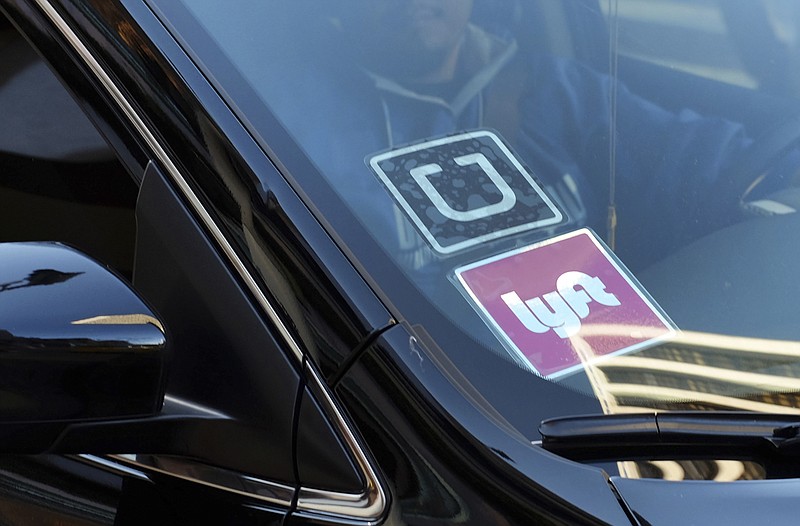 FILE - In this Jan. 12, 2016 file photo, a ride share car displays Lyft and Uber stickers on its front windshield in downtown Los Angeles, Calif.  Ride-hailing giants Uber and Lyft have launched subscription plans promising savings for trips to the gym, to work or around town. The ride-hailing companies stand to gain by increasing customer loyalty in a competitive market and securing more predictable revenue at a time when both companies are heading to an initial public offering.   (AP Photo/Richard Vogel, File)