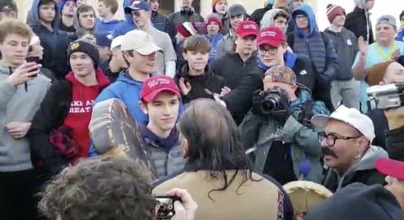 In this Friday, Jan. 18, 2019 image made from video provided by the Survival Media Agency, a teenager wearing a "Make America Great Again" hat, center left, stands in front of an elderly Native American singing and playing a drum in Washington. The Roman Catholic Diocese of Covington in Kentucky is looking into this and other videos that show youths, possibly from the diocese's all-male Covington Catholic High School, mocking Native Americans at a rally in Washington. (Survival Media Agency via AP)

