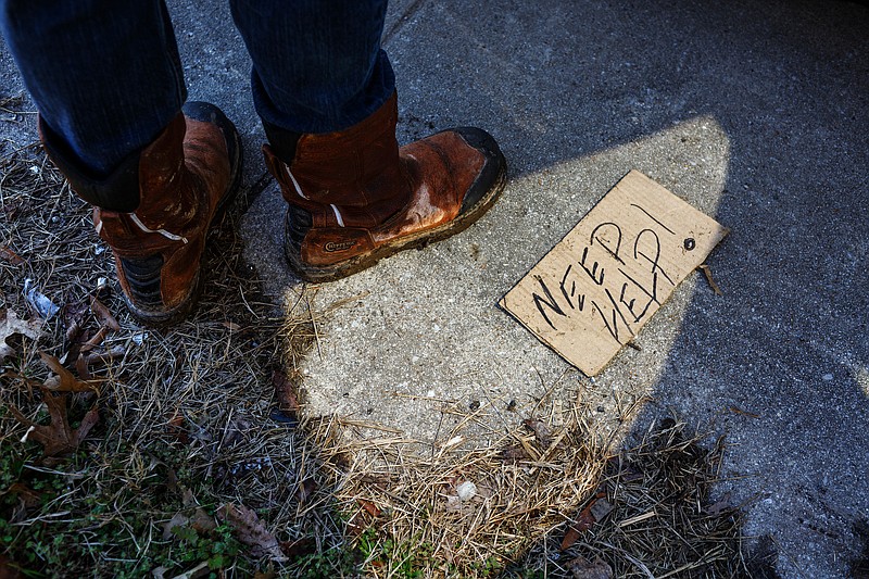 A panhandling sign is seen on the sidewalk as Teagan Buckner exits a vehicle while conducting an annual Point In Time Count of the city's homeless population on Friday, Jan. 25, 2019, in Chattanooga, Tenn. Service providers and volunteers conducted the PIT count, which surveys individuals experiencing homelessness in order to better target services to meet their needs, on Thursday night and Friday morning.