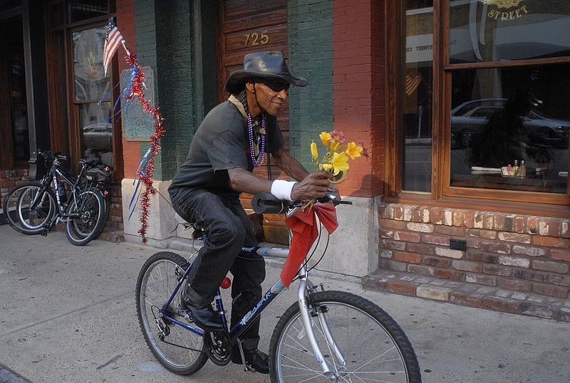 In this 2010 staff file photo, Oterius "Sandy the Flower Man" Bell rides down Cherry Street while making his rounds selling and giving away flowers in area bars and restaurants.