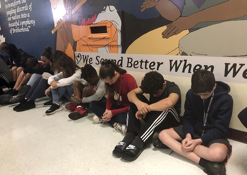 Students at Seminole Middle School in Plantation, Fla., participate in a moment of silence Thursday, Feb. 14, 2019, for the 14 students and three staff members killed one year ago at nearby Marjory Stoneman Douglas High School. They are sitting in front of a new mural depicting musicians from throughout the world that was dedicated to the shooting victims. (AP Photo/Terry Spencer)