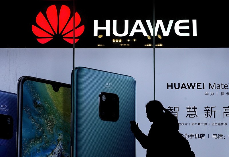 FILE - In this Dec. 11, 2018, file photo, a woman browses her smartphone as she walks by a Huawei store at a shopping mall in Beijing. China's government has accused Washington of trying to block its industrial development after Vice President Mike Pence said Chinese tech giant Huawei and other telecom equipment suppliers are a security threat. (AP Photo/Andy Wong)

